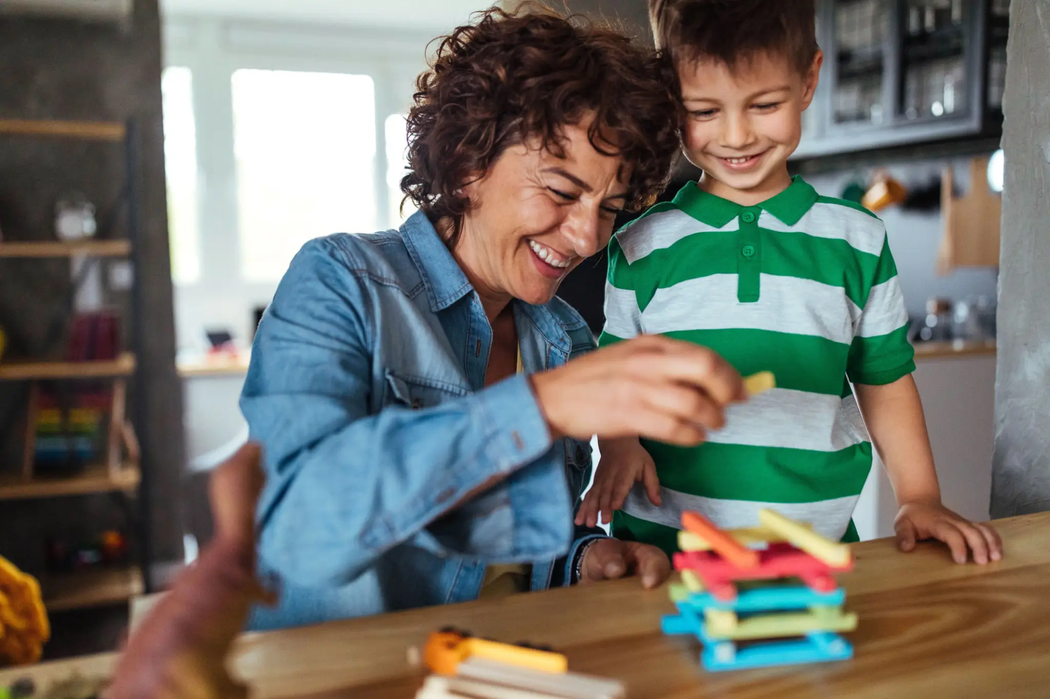 A smiling woman and boy building with colorful blocks indoors.