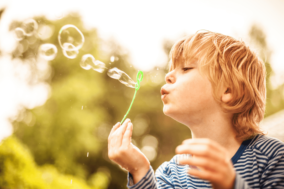 Child blowing bubbles outdoors in sunlight.