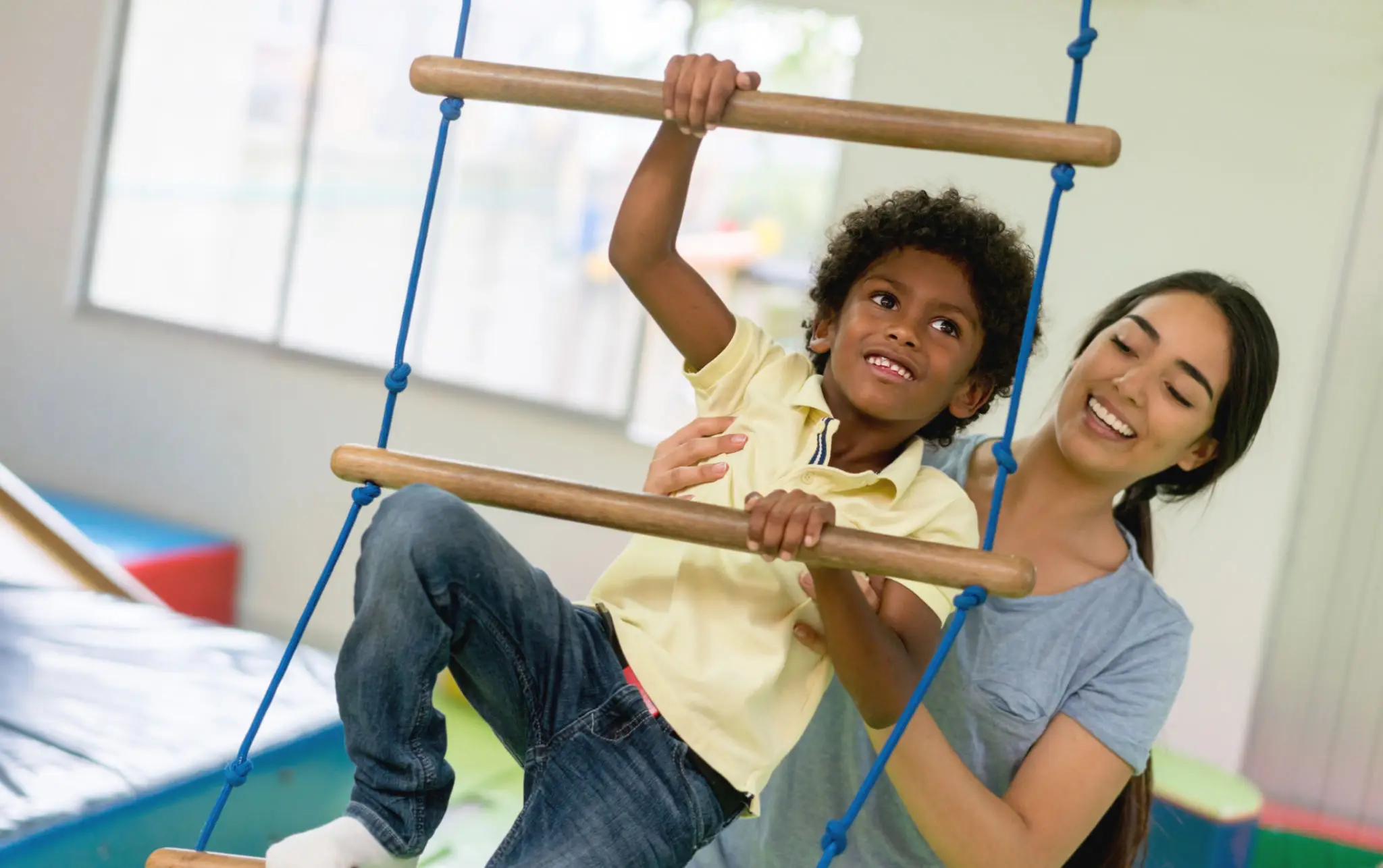 Child climbing playground ladder with adult support indoors.