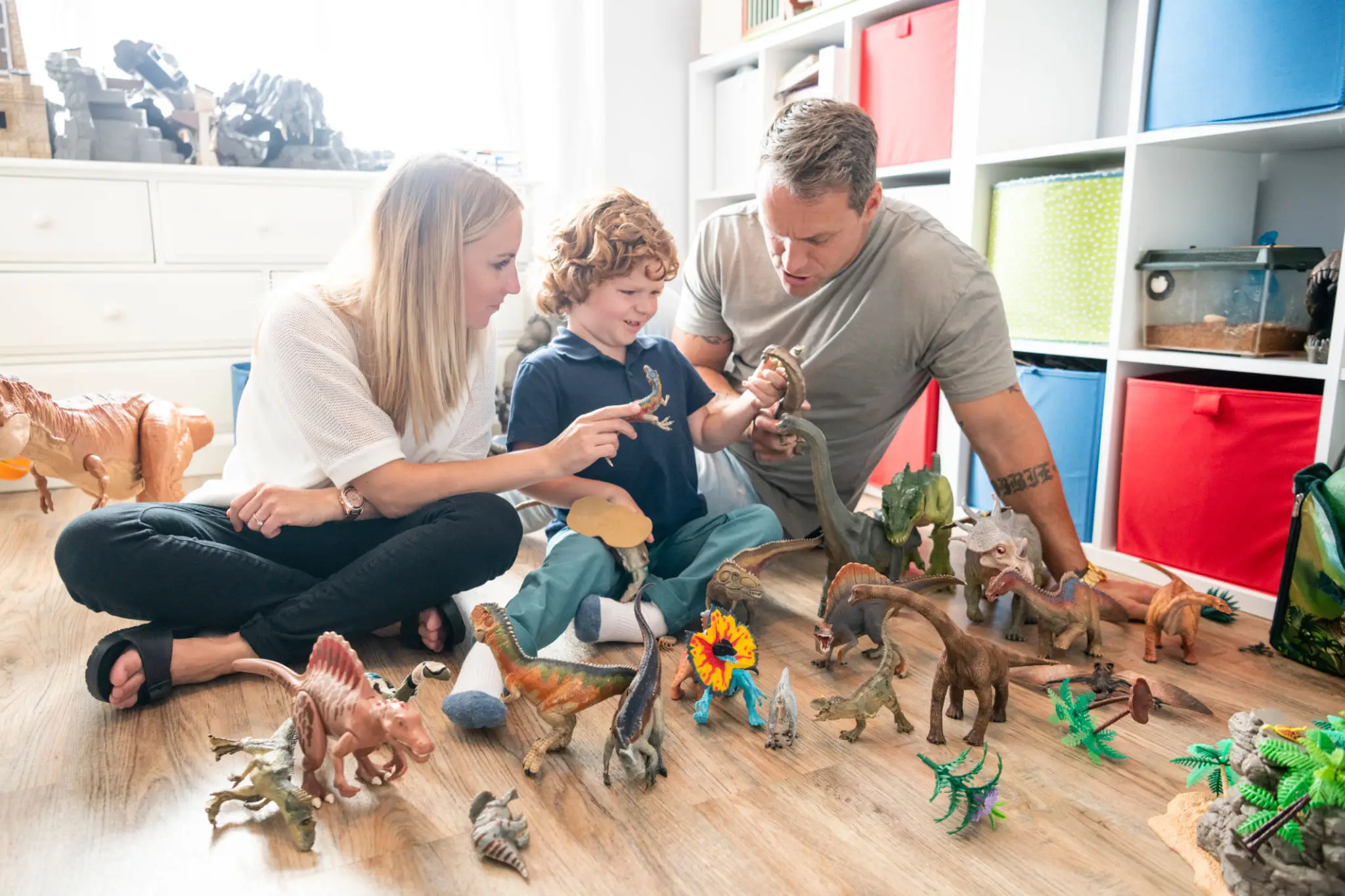 Family playing with dinosaur toys on the floor.