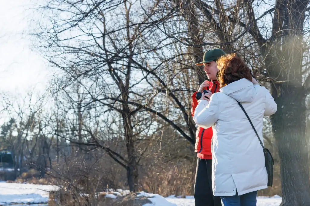 Two people dressed warmly in winter coats outdoors in a snowy, wooded area.