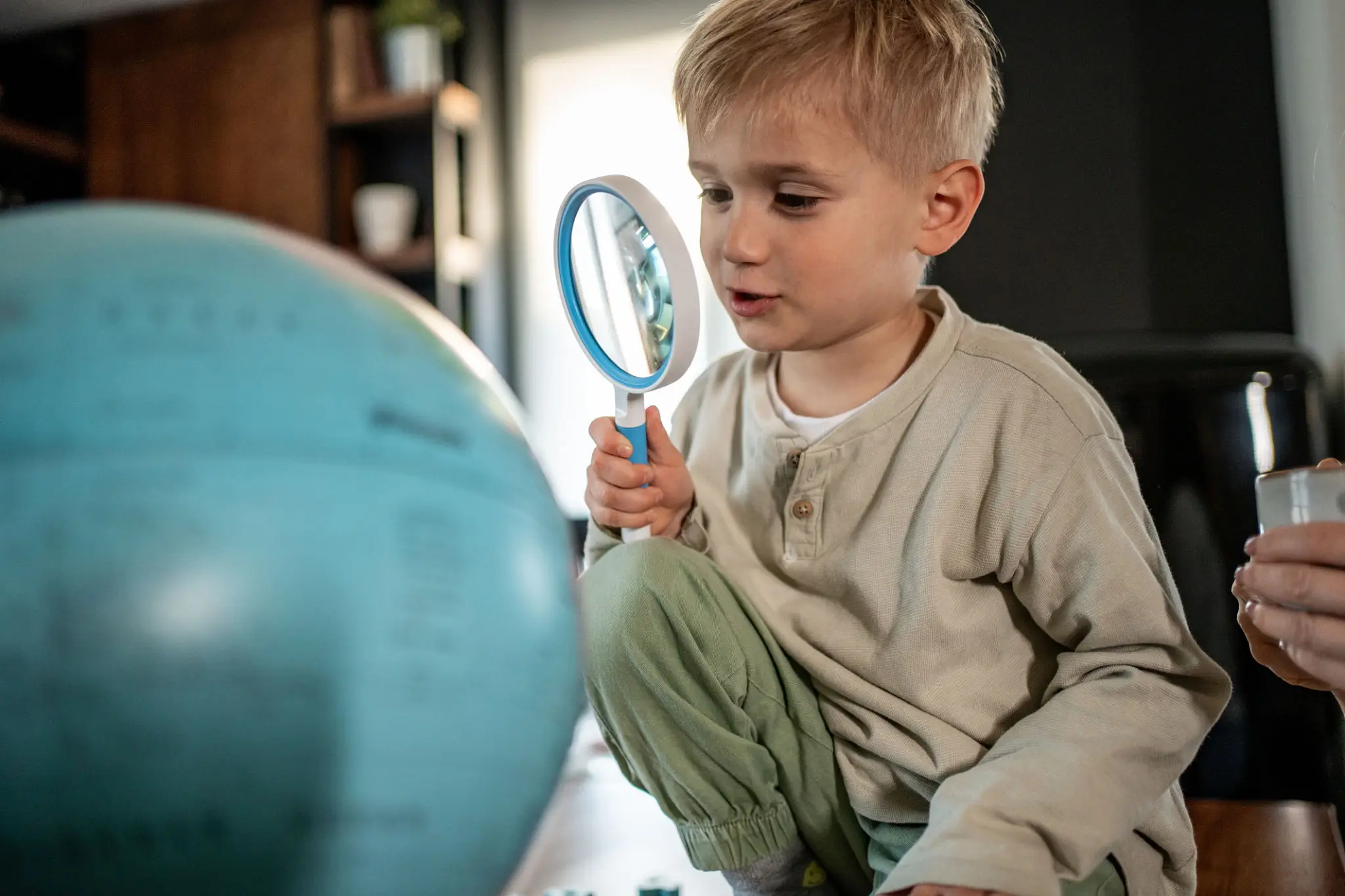 A young boy examining a globe with a magnifying glass indoors.